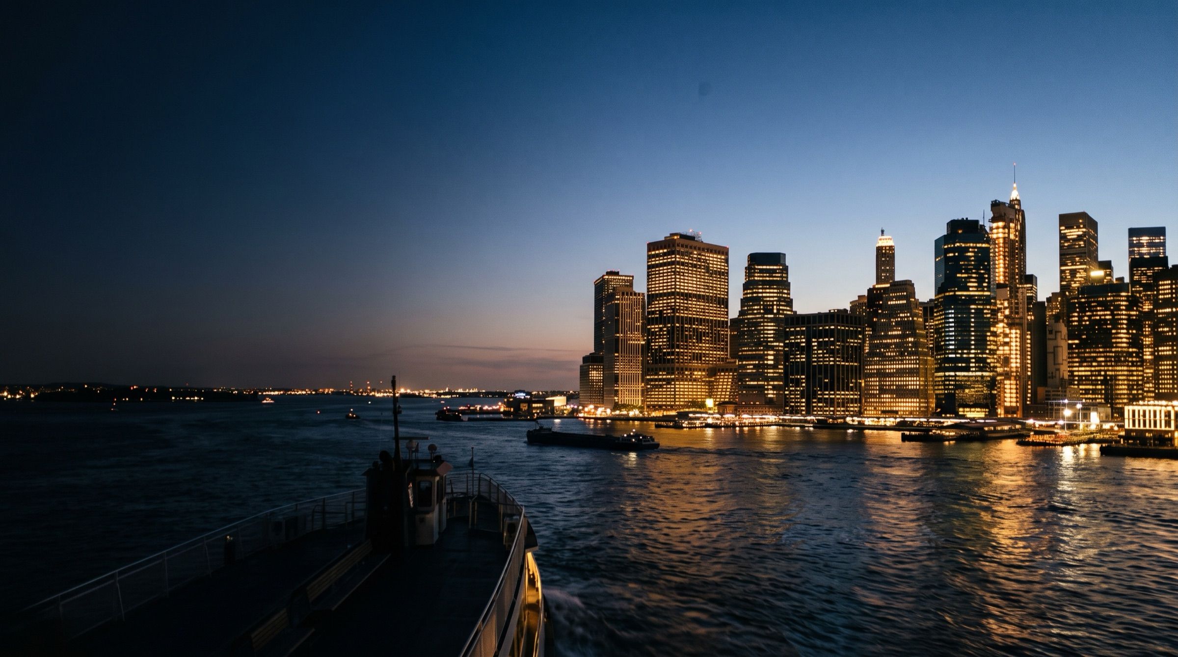 The Manhattan skyline at dusk seen from the river, warm windows, deep blue sky