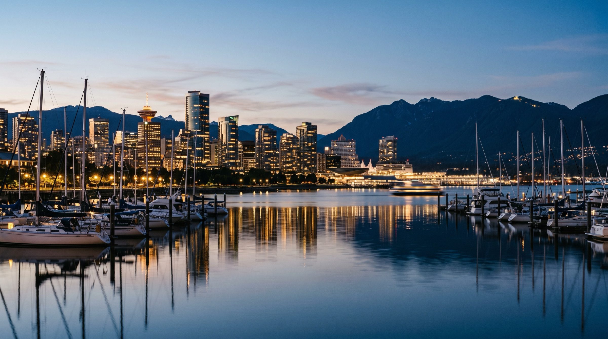 Vancouver harbour at dusk with moored sailboats, the city skyline and North Shore mountains