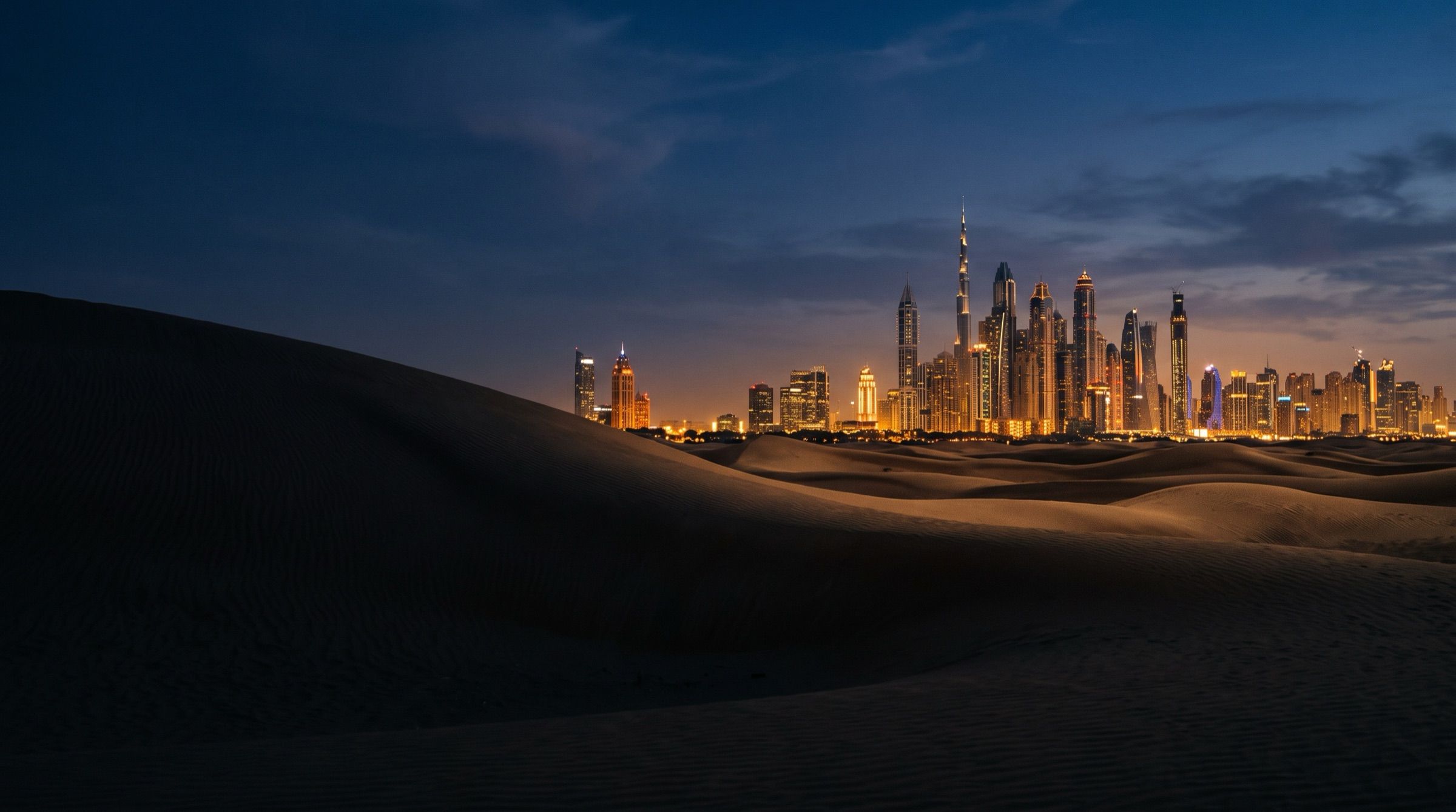 The Dubai skyline at blue hour seen from the edge of the desert dunes