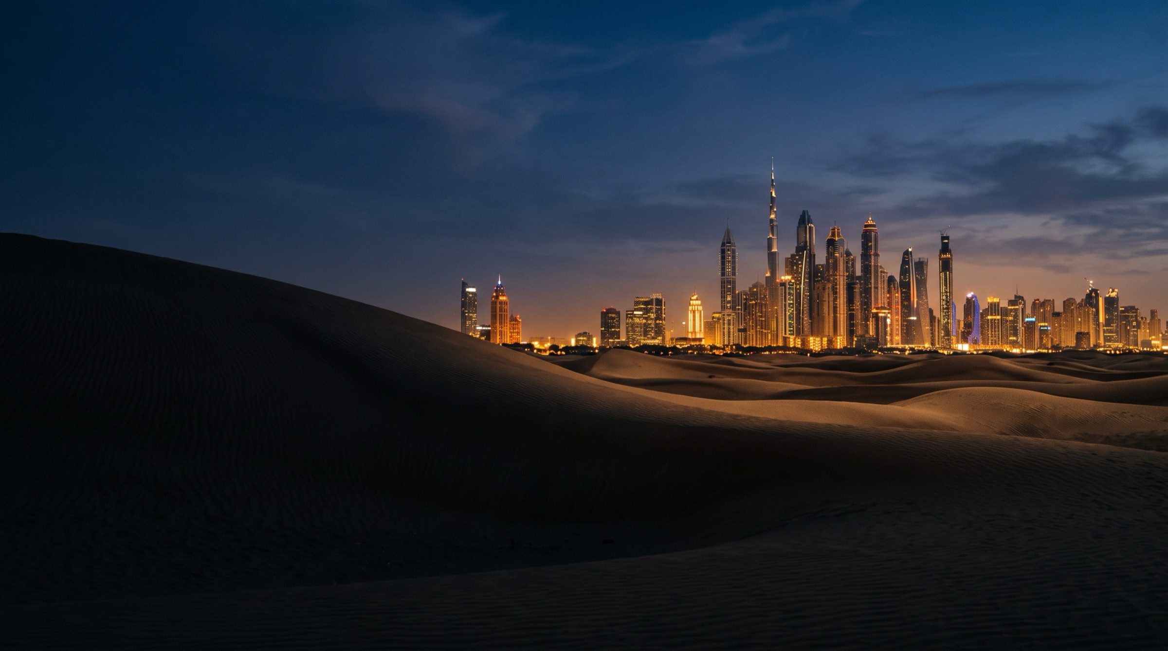 The Dubai skyline at blue hour seen from the edge of the desert dunes