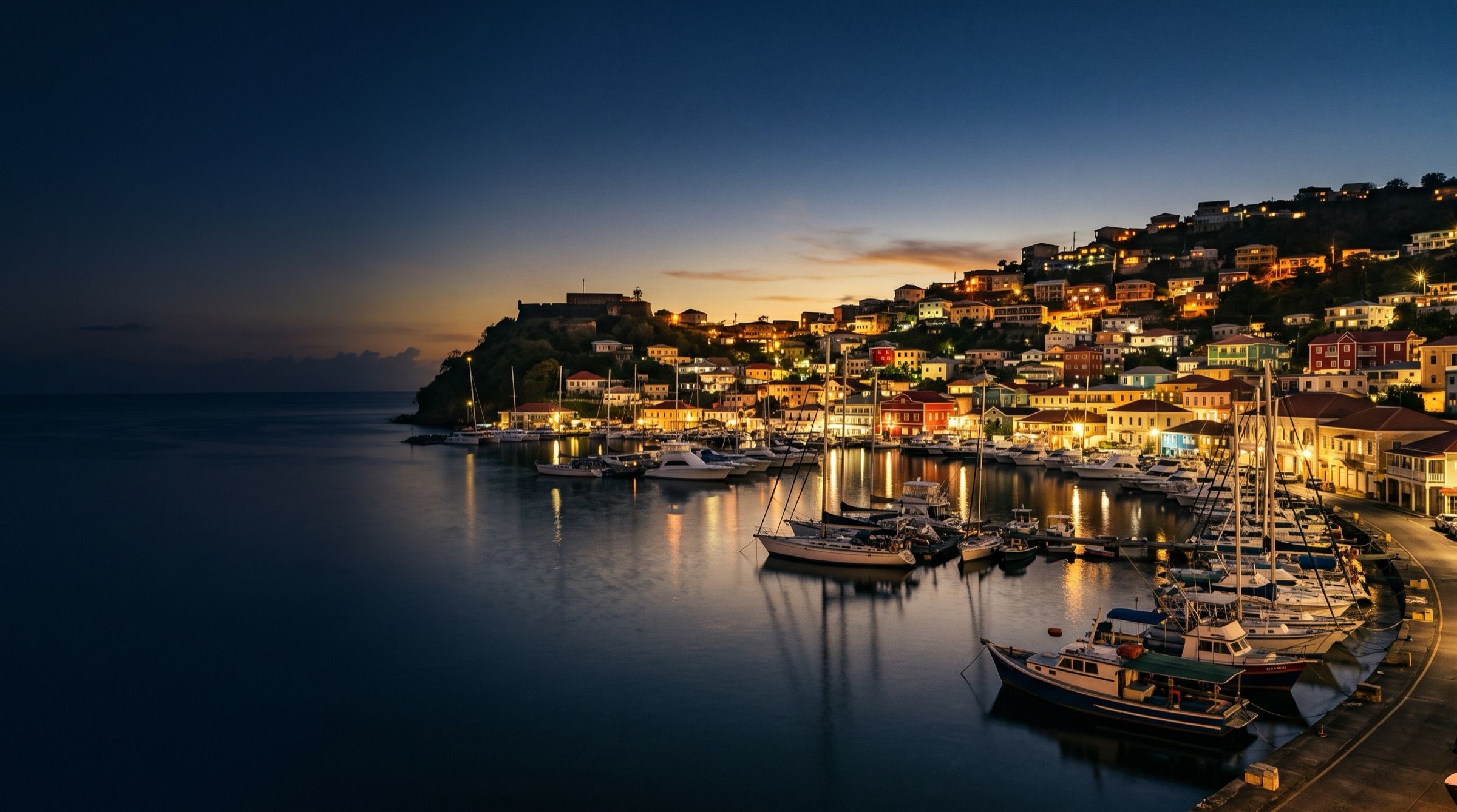 St George's harbour in Grenada at dusk, colourful hillside houses, boats on calm water