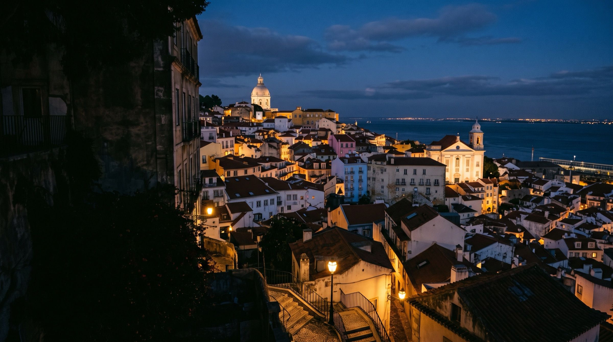 The Alfama district of Lisbon at dusk overlooking the Tagus, warm streetlights, church domes