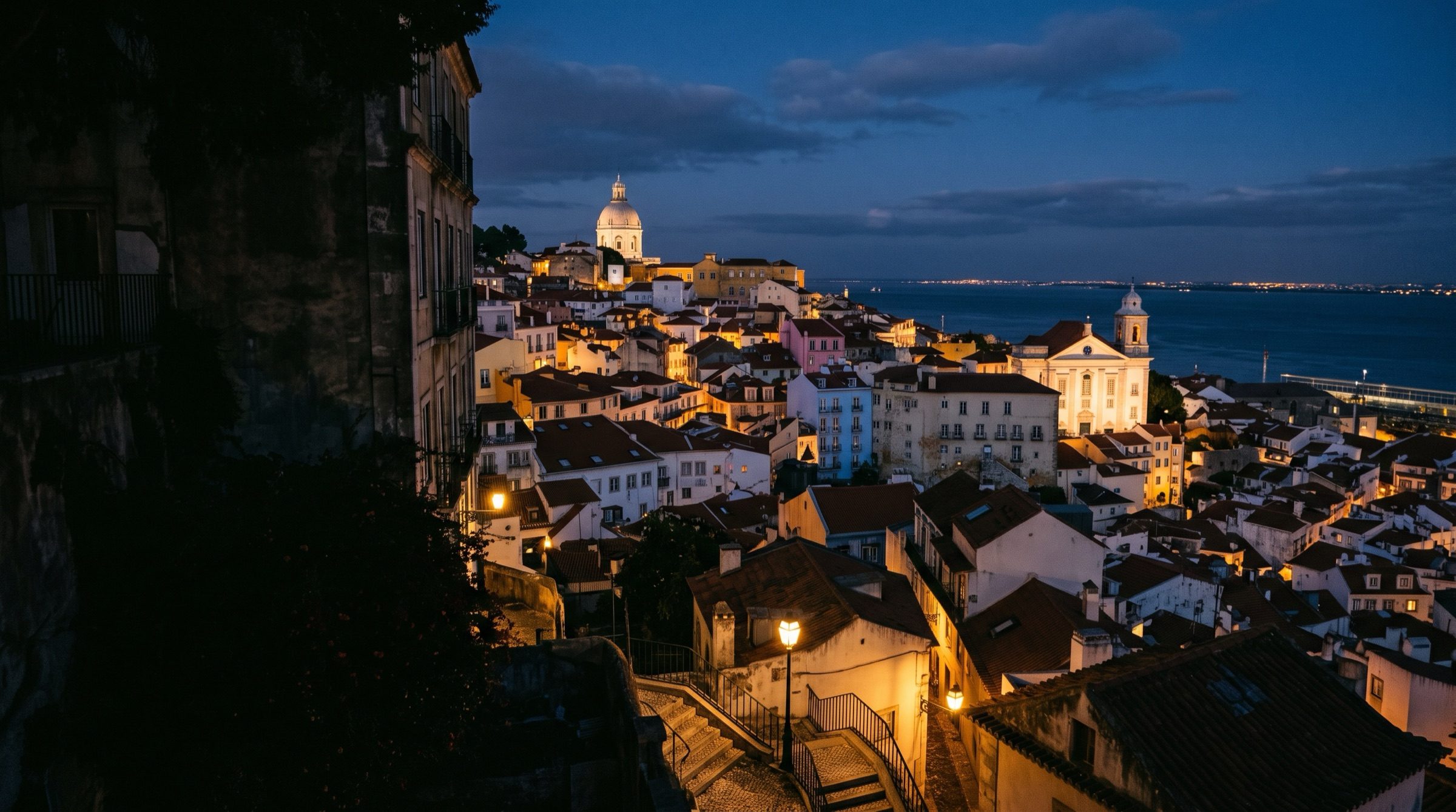 The Alfama district of Lisbon at dusk overlooking the Tagus, warm streetlights, church domes