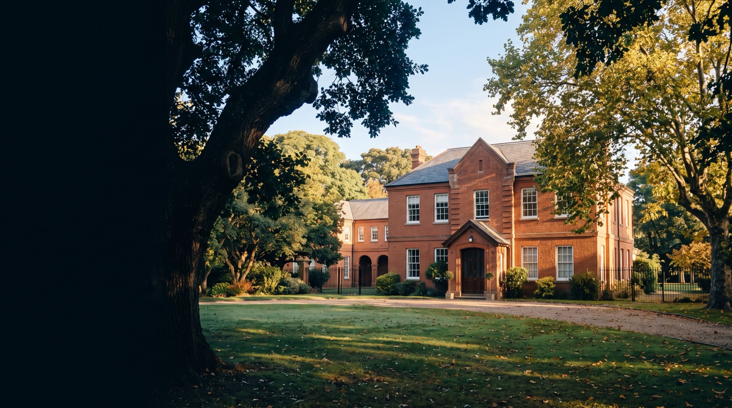 A red-brick British-style school building with green lawns and old trees in suburban Buenos Aires, morning light