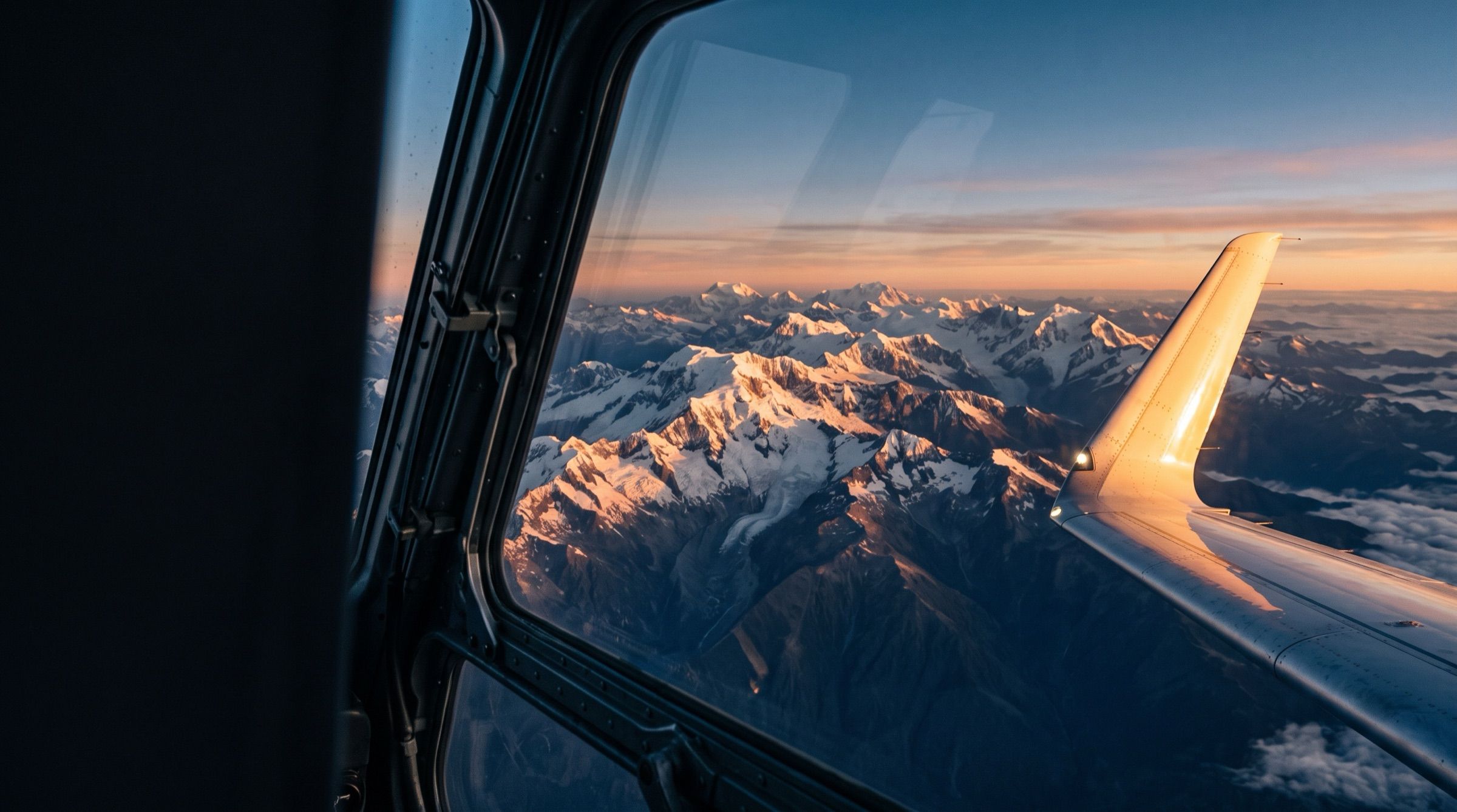 The snow-capped Andes seen from an airplane window at sunrise, wing tip catching golden light