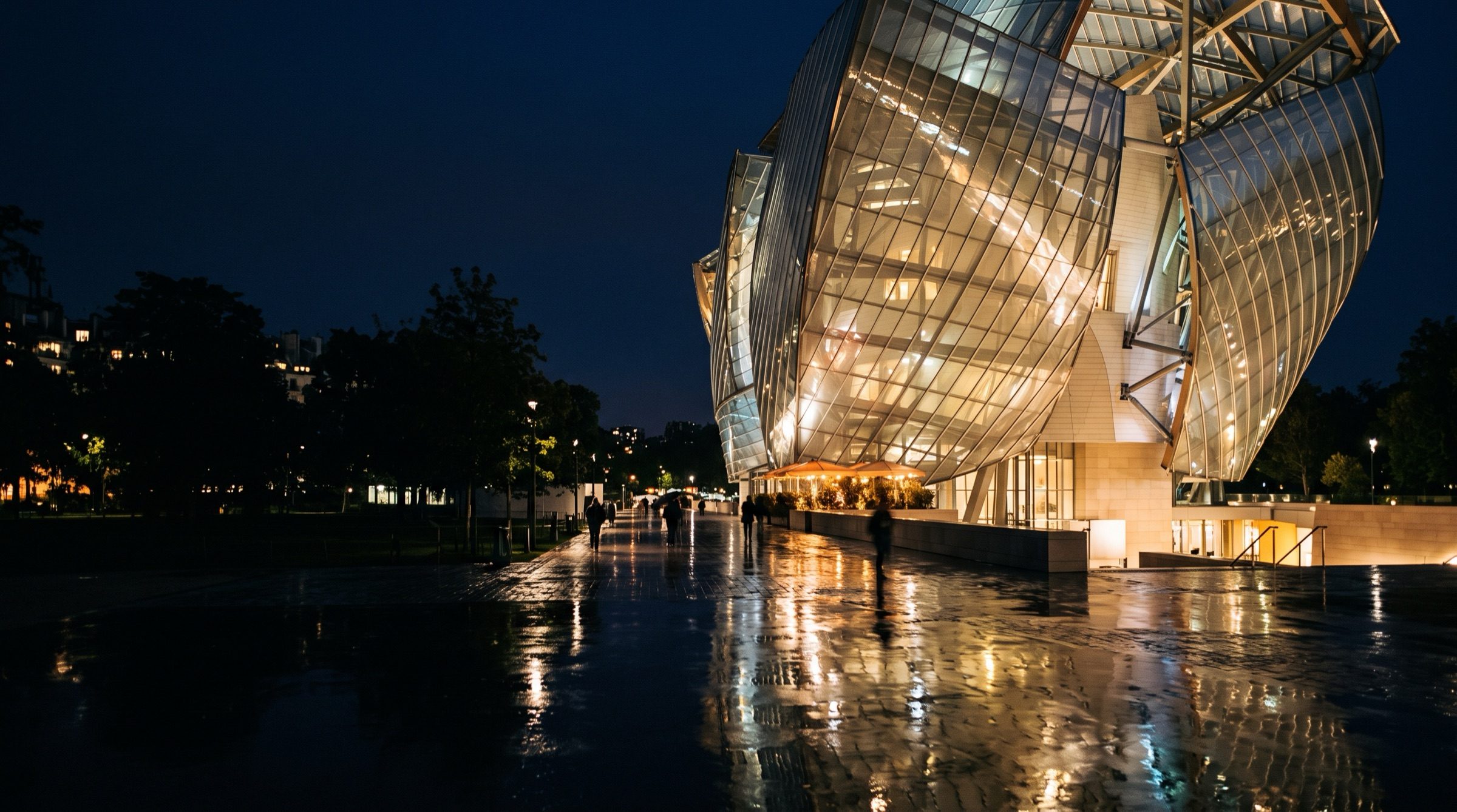 A modern glass institutional building at night in Paris with reflections in wet pavement, cool and warm light