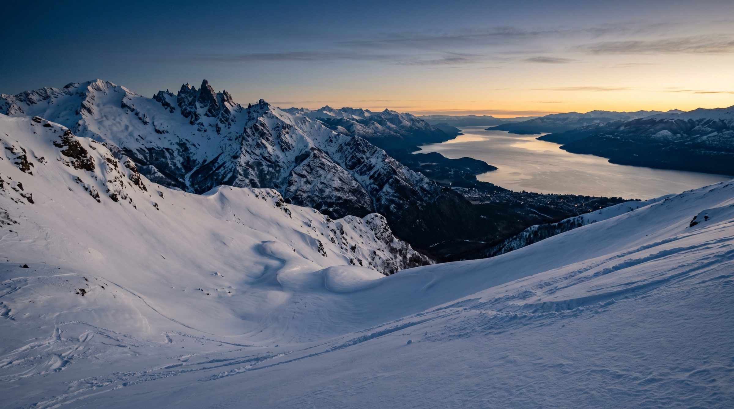 A snowy Andes ski slope at Cerro Catedral above Bariloche at first light, untouched powder, a lake far below